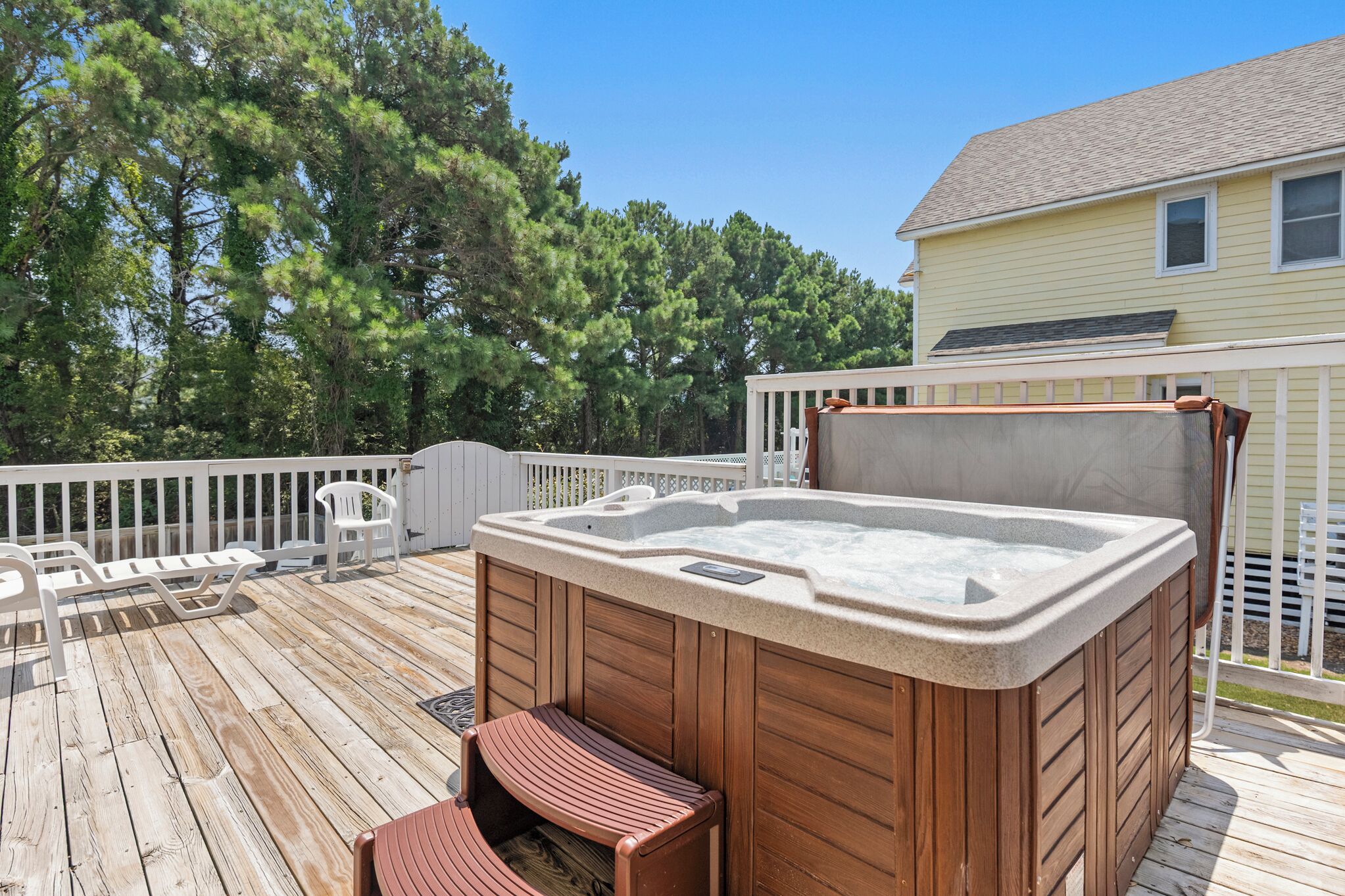Un bain à remous sur une terrasse en bois, avec vue sur une maison et des arbres.