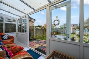 Ein Wintergarten mit Glastür, der auf eine Terrassenfläche mit Korbstuhl und Kissen führt.