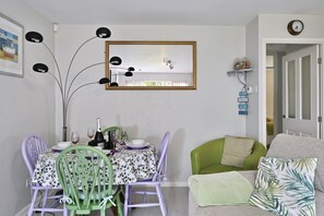 Un comedor con una mesa dispuesta para dos personas, un sillón verde y un sofá con cojines estampados.