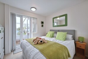 A hotel room with a bed, a green mirror, a nightstand, and a view through the door. - Historic Wiltshire Garden Cottage (Winchelsea)