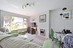 Ein Wohnzimmer mit Sofa, Fernseher, Kamin und Essbereich mit Tisch für zwei Personen.