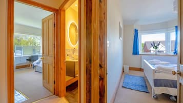 A hotel room with a wooden door, a bathroom with a mirror, a bed with a blue rug, and a window with curtains.