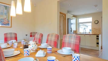A dining area with a wooden table set for a meal, featuring a coffee pot, teapot, and various mugs and plates.