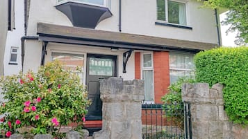 A two-story house with a stone wall in front, a black gate, and a red brick section on the lower level.