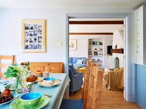 A dining area with a wooden table set for a meal, a blue sofa, and a bookshelf in the background. - Coastal Stay Near Coast Path (Kingsbridge)