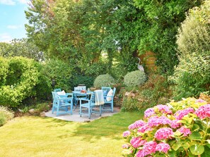 An outdoor seating area with a table and chairs, surrounded by lush greenery and flowering plants. - Coastal Stay Near Coast Path (Kingsbridge)