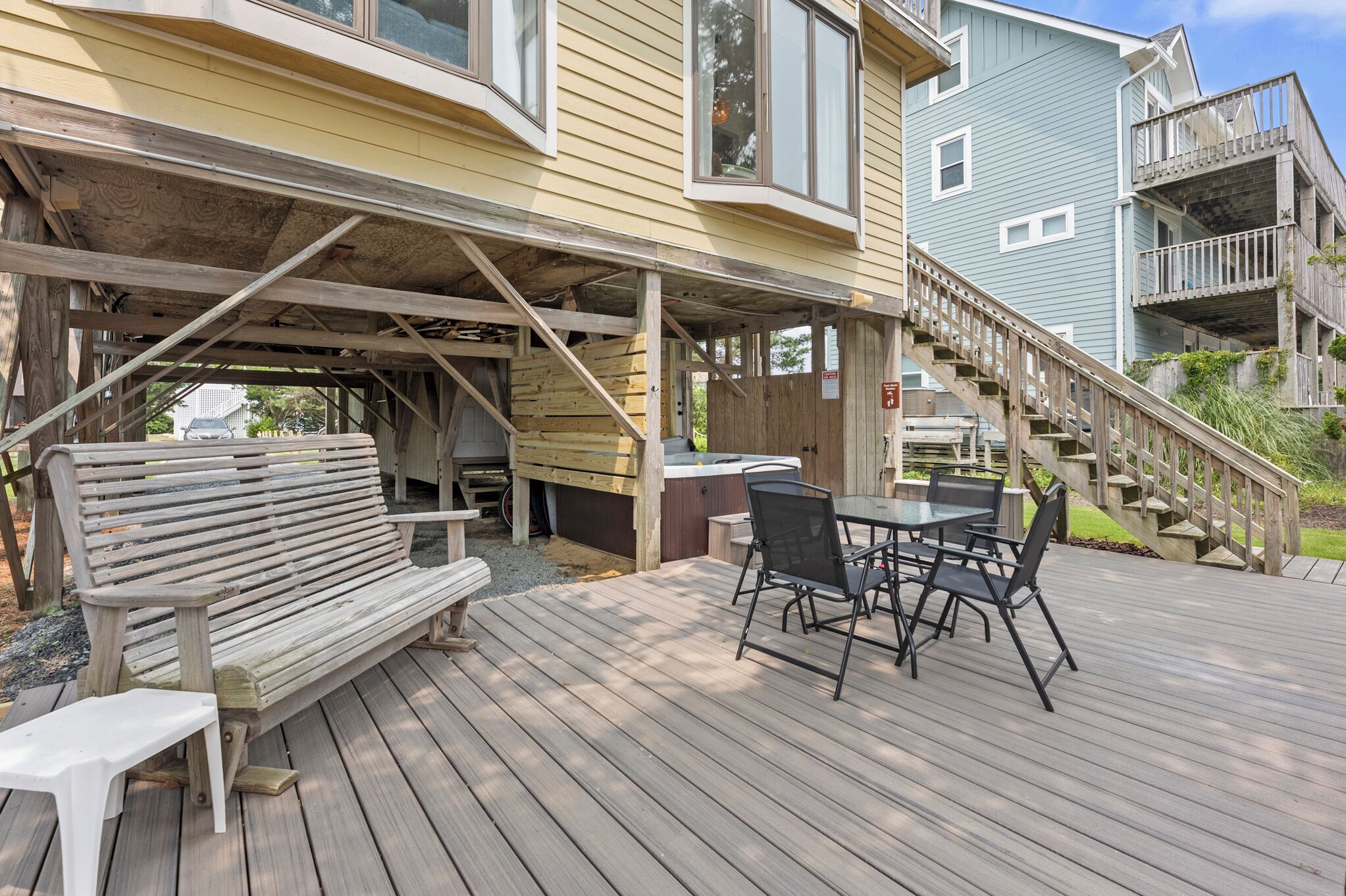 A wooden deck with outdoor furniture, a hot tub, and a staircase leading to a second-story balcony.