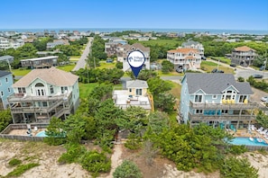 A residential area with houses, a swimming pool, and a beach in the background.