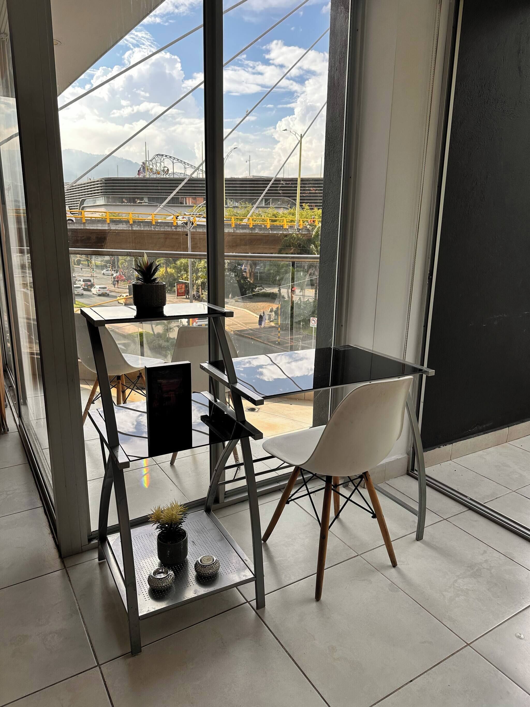 Una habitación moderna con un gran ventanal, una mesa de vidrio, dos sillas y una pequeña planta en maceta.