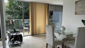 Un moderno comedor con una mesa y sillas de vidrio, vista a zonas verdes exteriores y una puerta corredera de vidrio.