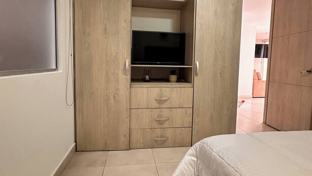 Un dormitorio con una cama, un televisor en un estante y un armario.
