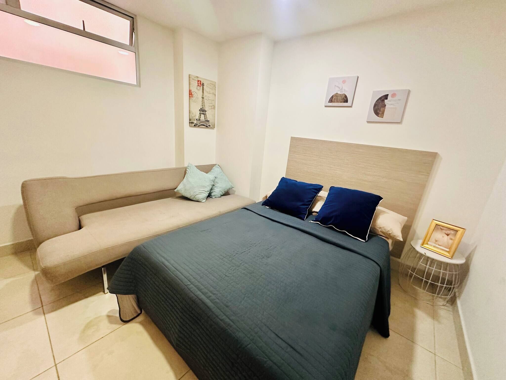 Un dormitorio con cama, sofá, mesita de noche y decoración en la pared.