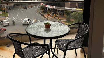 Uma varanda com mesa e cadeiras de vidro, com vista para uma rua movimentada com uma ponte e edifícios.