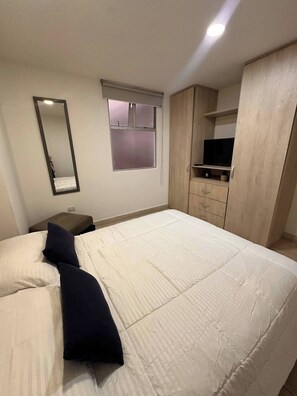 Un dormitorio con cama, mesita de noche, espejo, ventana, armario y televisión.