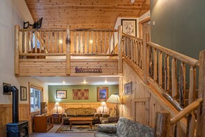 A wooden interior with a loft bedroom, a staircase, and a living area with a sofa and lamps.