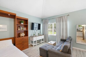 A bedroom with a bed, a wooden wardrobe, a desk with a TV, a grey sofa, and a window with curtains. - 7 Mi to Historic Dtwn! New Port Richey Cottage (New Port Richey)