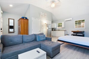 Um espaço compacto com sofá, cama, cozinha compacta e ventilador de teto.