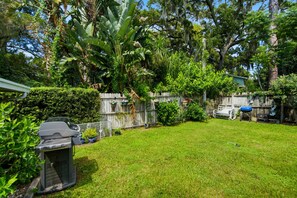 Un jardin avec un barbecue, une clôture en bois et différentes plantes.
