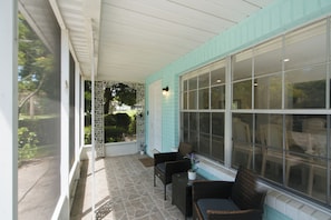 Eine überdachte Veranda mit Korbmöbeln und einem großen Fenster.