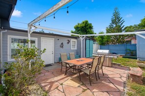 Eine Terrasse mit Tisch und Stühlen, einem Grill und einem überdachten Bereich mit Lichterketten.