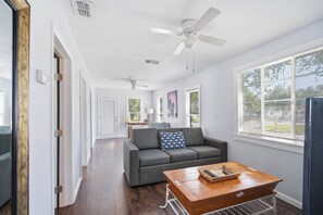 Ein modernes Wohnzimmer mit einem grauen Sofa, einem Holztisch und einem Deckenventilator.