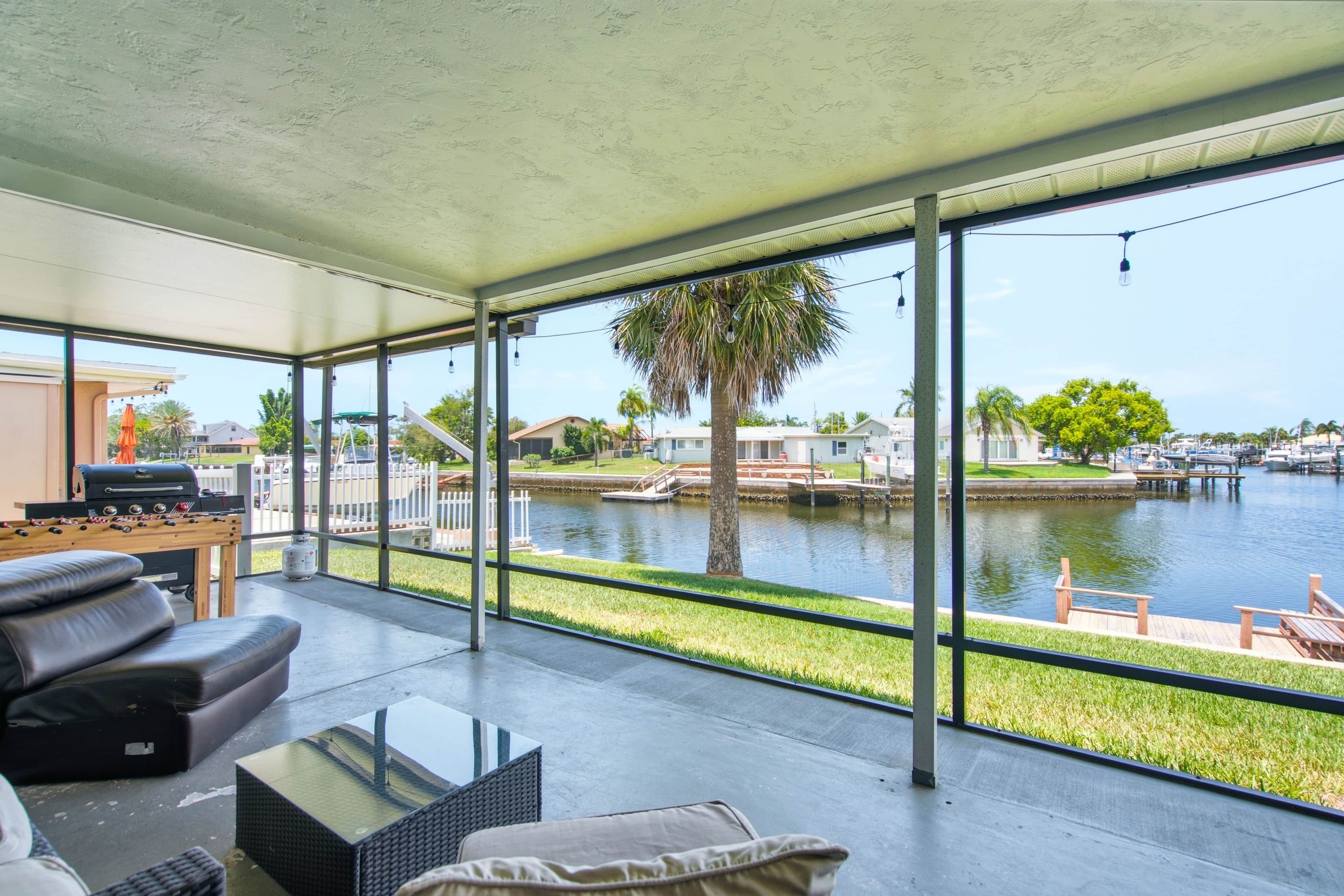 A spacious balcony with a view of a body of water, a grill, and a seating area with a glass table.