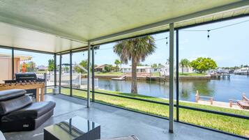 A spacious balcony with a view of a body of water, a grill, and a seating area with a glass table.