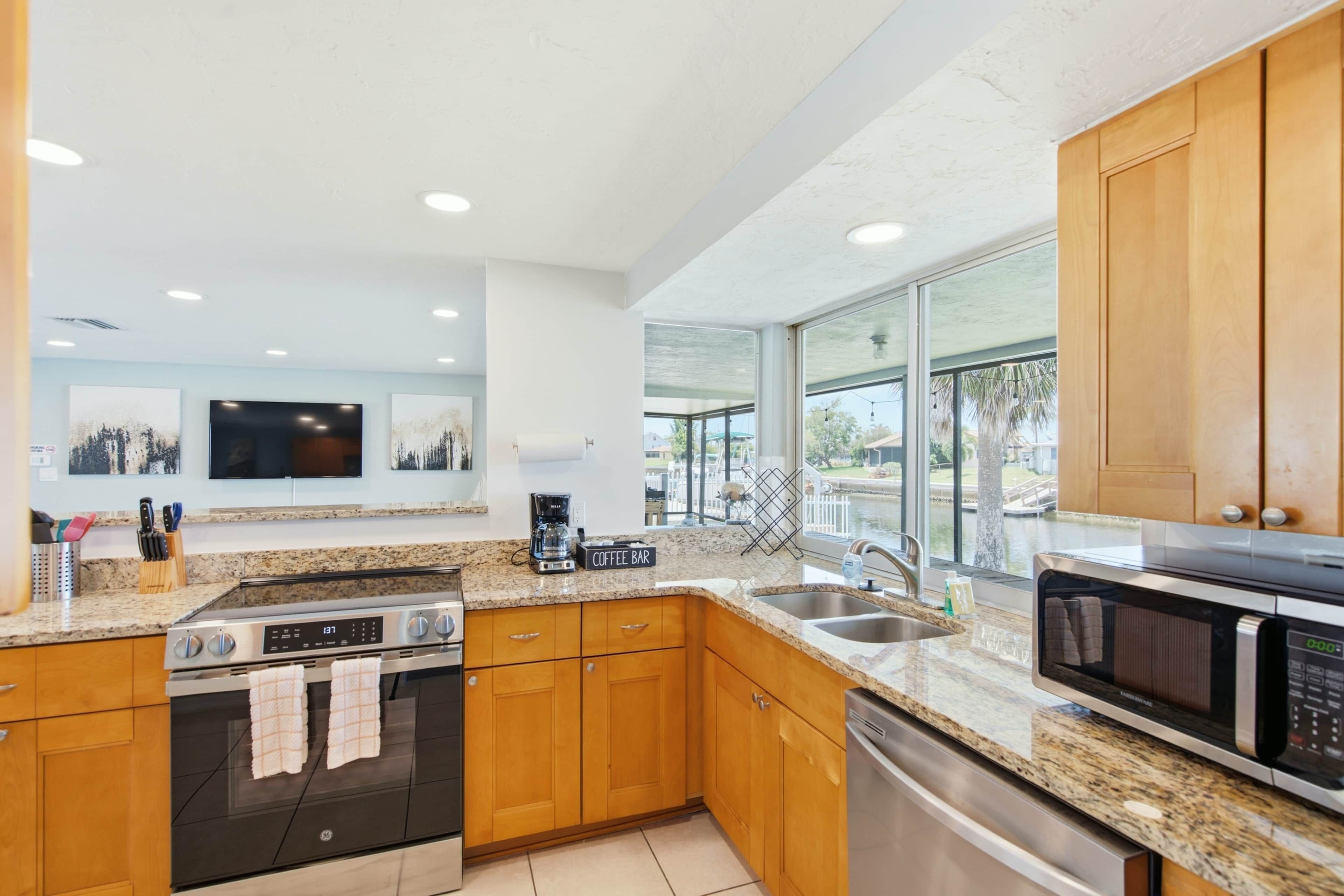 A modern kitchen with granite countertops, wooden cabinets, stainless steel appliances, and a view of a water body.
