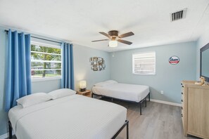 A hotel room with two beds, a ceiling fan, a window with curtains, a wall-mounted light, and a sign indicating the hotel's service.