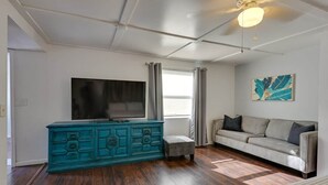 A living room with a teal cabinet, a flat-screen TV, a gray sofa, and a ceiling fan. - Updated Studio 1 Mi to Dtwn NPR & Cotee River! (New Port Richey)
