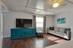 Ein Wohnzimmer mit einem türkisblauen Schrank, einem Flachbildfernseher, einem grauen Sofa und einem Deckenventilator.