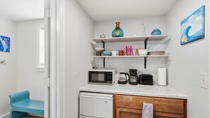 A compact kitchen with a microwave, coffee maker, and toaster on the counter, a small refrigerator, and shelves with various kitchenware. - Updated Studio 1 Mi to Dtwn NPR & Cotee River! (New Port Richey)