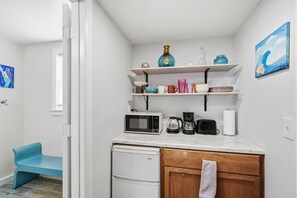 Eine kompakte Küche mit einer Mikrowelle, einer Kaffeemaschine und einem Toaster auf der Arbeitsfläche, einem kleinen Kühlschrank und Regalen mit diversen Küchenutensilien.