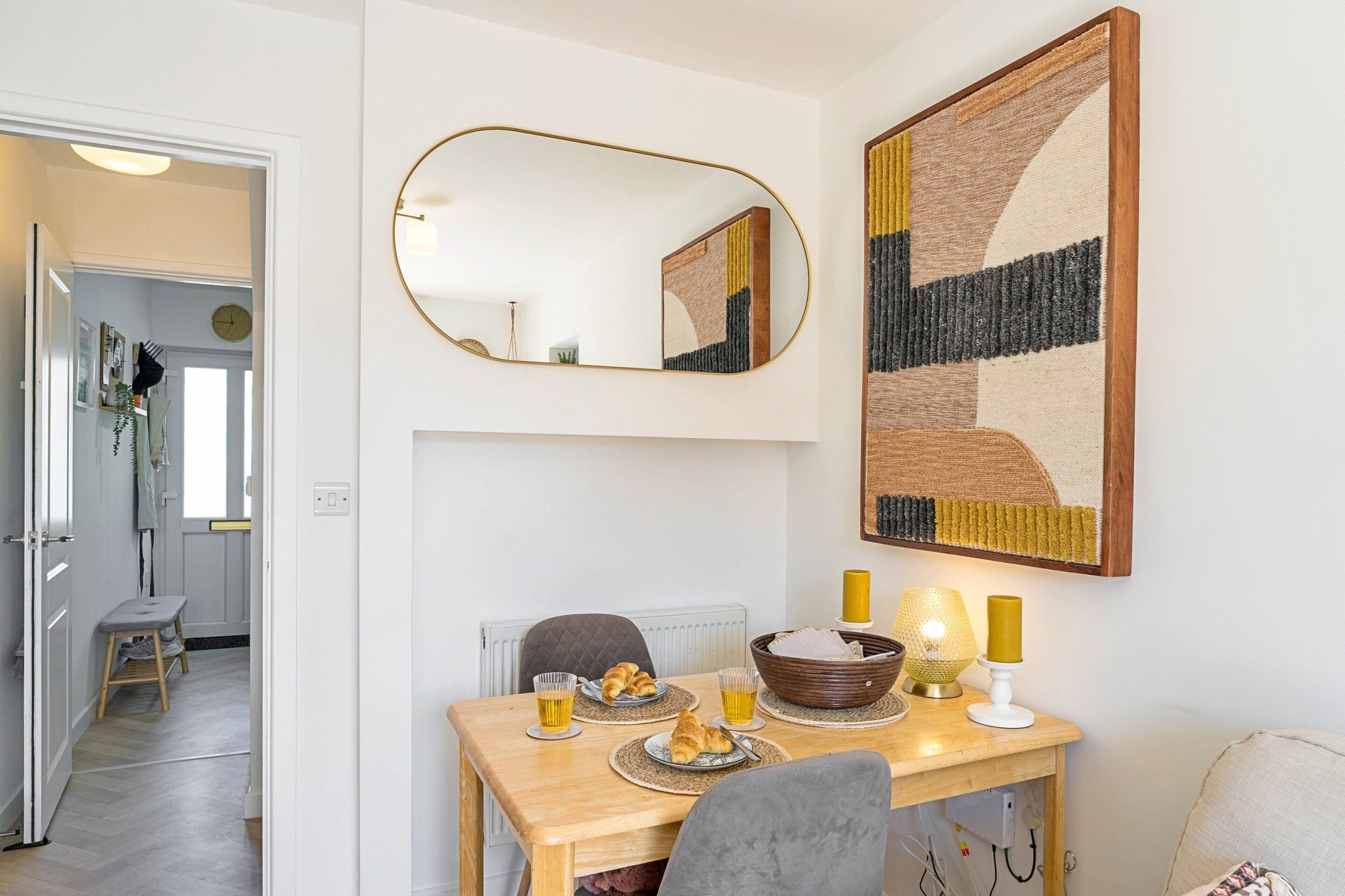 Un comedor con una mesa dispuesta para dos, un espejo y un cuadro abstracto grande en la pared.