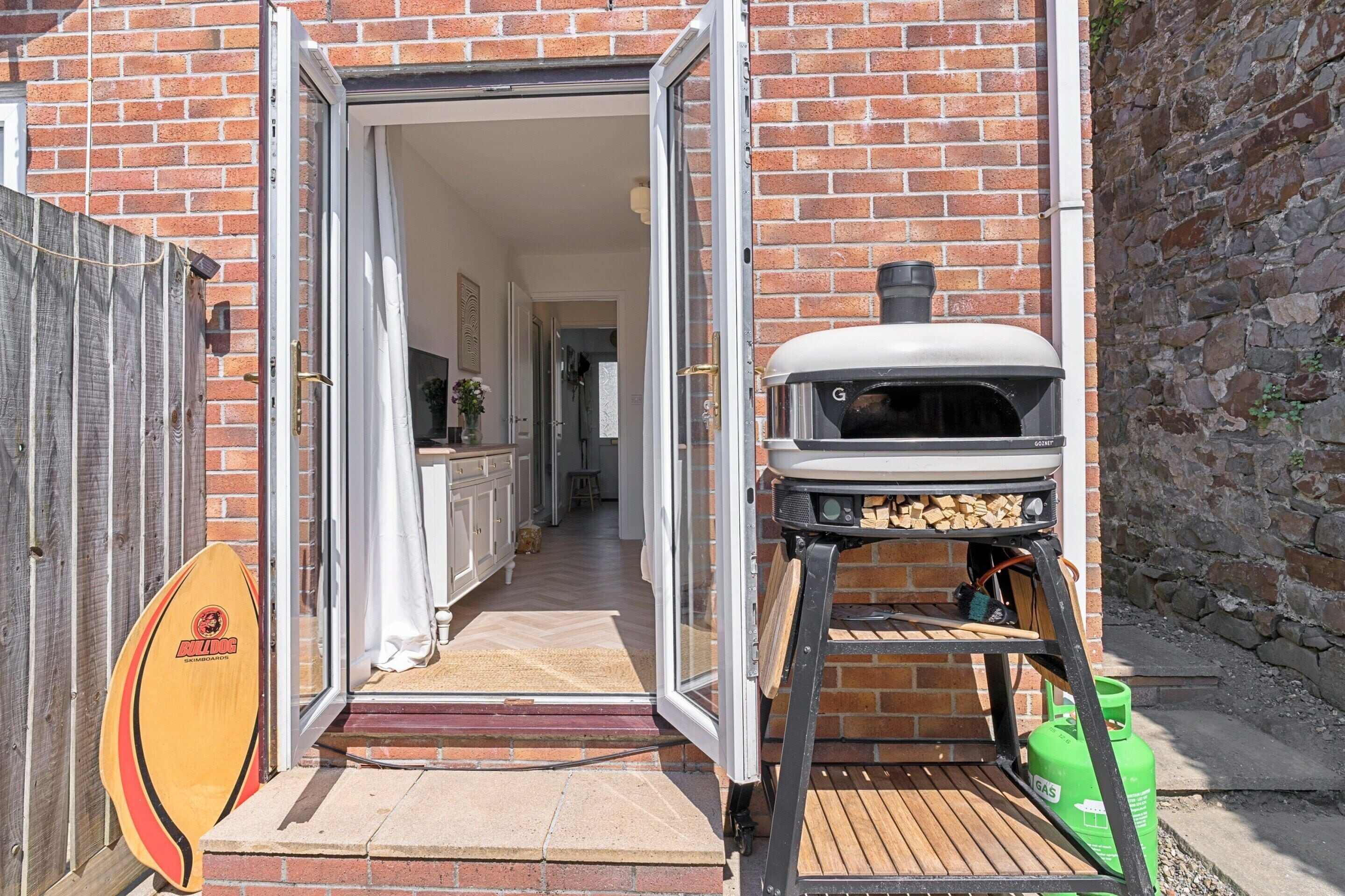 A brick building with a wooden deck, a barbecue grill, and a surfboard.