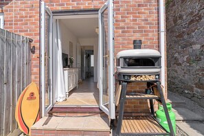 Ein Backsteinhaus mit einer Holzterrasse, einem Grill und einem Surfbrett.