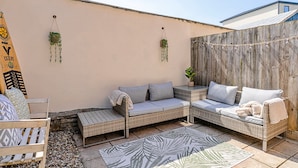 Un espace extérieur accueillant, aménagé avec des meubles en osier, un tapis à motifs et des plantes suspendues.