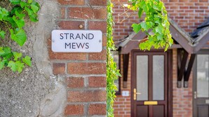 Un mur de briques avec une enseigne indiquant « STRAND MEWS » et une porte en arrière-plan.