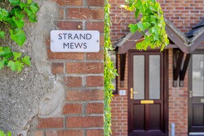 Eine Ziegelmauer mit einem Schild, auf dem 'STRAND MEWS' steht, und einer Tür im Hintergrund.