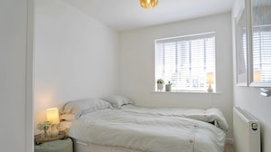 Une chambre à coucher comprenant un lit, une table de chevet, une lampe, une fenêtre, un radiateur et une petite plante en pot.