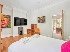 Ein Schlafzimmer mit Bett, Fernseher, Kamin, Sessel und Bildern an den Wänden.