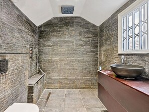 Ein Badezimmer mit Steinwand, einem großzügigen Waschbecken und einem Fenster mit geometrischem Muster.