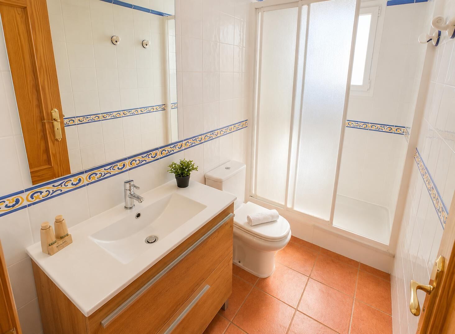 A bathroom with a white sink, wooden vanity, a toilet, and a shower area.