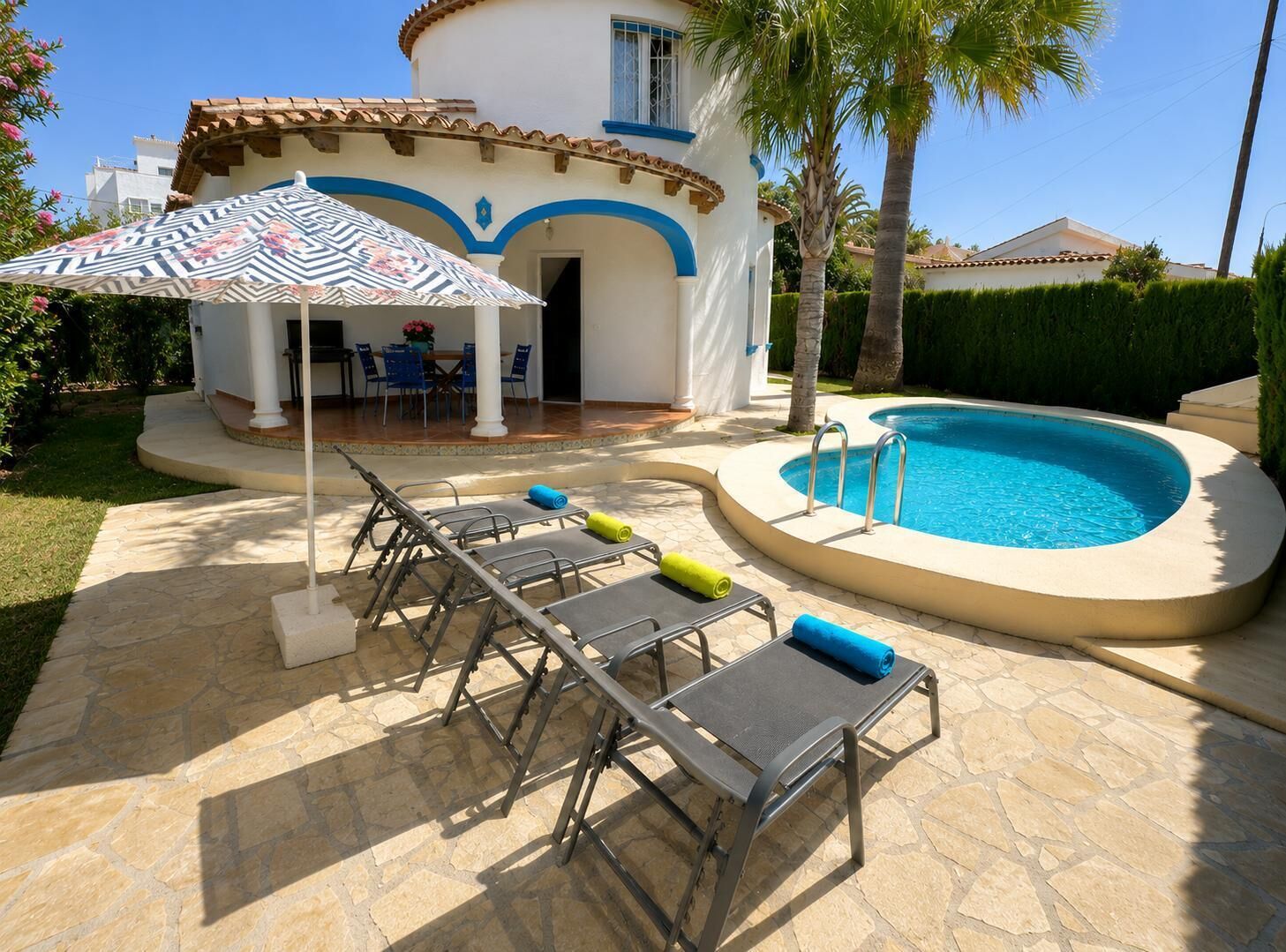 Un área junto a la piscina con sillones reclinables, un porche cubierto y una pileta.