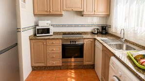 A compact kitchen with wooden cabinets, a microwave, an oven, a sink, and a washing machine. - Villa Molins Tauro - Three Bedroom Villa, Sleeps 6 (Dénia)
