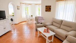 A living room with a sofa, a coffee table, a TV, a washing machine, and a dining area with chairs and a table. - Villa Molins Tauro - Three Bedroom Villa, Sleeps 6 (Dénia)