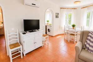 A living room with a TV, white furniture, a washing machine, and a dining area with chairs and a table. - Villa Molins Tauro - Three Bedroom Villa, Sleeps 6 (Dénia)