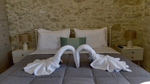 Quarto com parede de pedra, cama com roupa de cama branca, duas mesas de cabeceira com luminárias e um travesseiro decorativo verde.