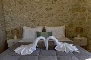 Ein Schlafzimmer mit Steinwand, einem Bett mit weißen Leinentüchern, zwei Nachttischen mit Lampen und einem grünen Zierkissen.