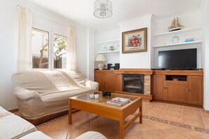 Uma sala de estar com sofá, mesa de centro, lareira, televisão e estante de livros.